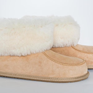 May include: A pair of tan suede ankle boots featuring a thick, plush white faux fur cuff around the top opening. The boots have a rounded toe, visible stitching along the vamp, and a textured tan rubber sole base for traction and support.