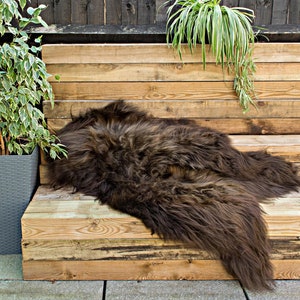 Könnte beinhalten: Ein brauner Schaffellteppich liegt auf einer Holzbank. Die Bank besteht aus wiederverwendeten Holzbrettern. Der Teppich ist weich und flauschig.