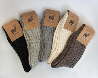 May include: Five pairs of alpaca wool socks in different colors: black, gray, white, brown, and beige. Each sock has a brown tag with the words "Alpaca Wool" and a small image of an alpaca.