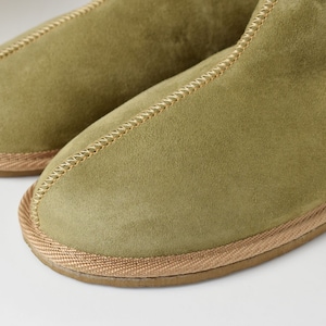 May include: A pair of green suede slippers with a brown trim around the edges.