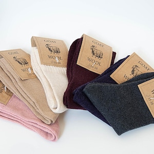 May include: A collection of folded wool socks in various colors, including pink, beige, white, burgundy, navy, and charcoal gray. Each pair has a tag with a goat illustration and the word "WOOL". The socks are sized 35-38.