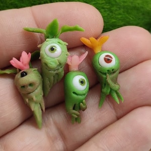 May include: Four small green and pink clay figurines, each with one large eye. The figurines are shaped like plants with stems and leaves.