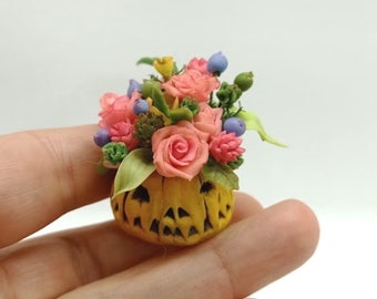 May include: A miniature ceramic pumpkin with a carved face, filled with a bouquet of pink and yellow roses, green leaves, and purple berries.