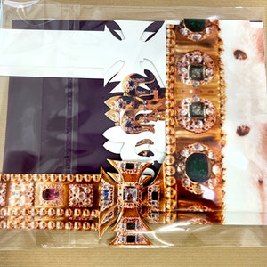 May include: A gold crown with green and red jewels, a white fur lining, and a gold cross with a purple background.