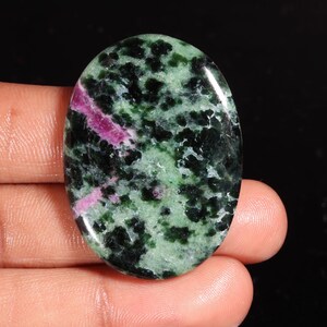 Op de afbeelding: Een ovaalvormige gepolijste edelsteen cabochon met een gevlekt patroon van diep bosgroen, licht saliegroen en levendige magenta-roze insluitingen over het gladde, reflecterende oppervlak van de steen.