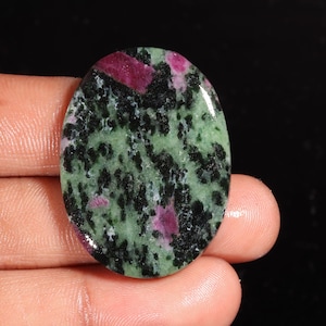 May include: An oval-shaped polished gemstone featuring a mottled pattern of deep forest green, black, and vibrant magenta-pink inclusions. The stone has a smooth, reflective surface with a high-gloss finish, showcasing a natural mineral composition.