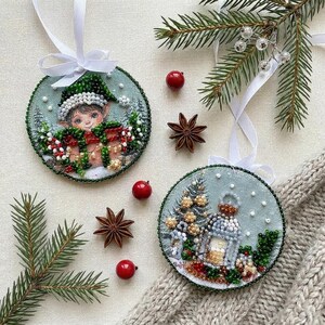 May include: Two circular Christmas decorations with beaded designs. One shows an elf with a gift, the other a winter scene with a lantern and Christmas tree. Star anise, red berries, and pine branches are also present.