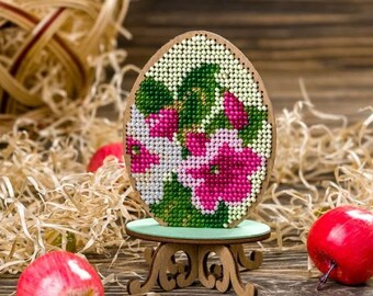 Può includere: Un ornamento per uova di Pasqua in legno con un motivo floreale. L'uovo è decorato con perline rosa, bianche e verdi ed è esposto su un supporto in legno.