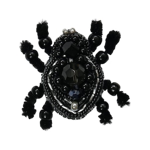 Puede incluir: Broche de escarabajo negro de cuentas con un gran cristal facetado en el centro. El escarabajo tiene patas peludas negras y está hecho con cuentas negras y plateadas.