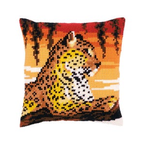 Puede incluir: Una almohada de punto de cruz con un leopardo acostado en una escena de puesta de sol con palmeras. El leopardo es marrón, amarillo y blanco con manchas negras. El fondo es naranja, rojo y amarillo.