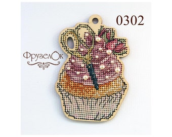 May include: A wooden cupcake ornament with pink frosting, white pearls, and a yellow bow. The ornament is decorated with a cross-stitch pattern and has the text "0302" printed on it.