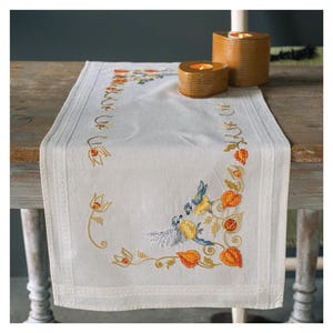 Pode incluir: Um corredor de mesa de linho branco com um design bordado de pássaros e folhas em tons de laranja, amarelo e azul. O corredor de mesa tem uma borda festonada e é perfeito para adicionar um toque de elegância a qualquer mesa.