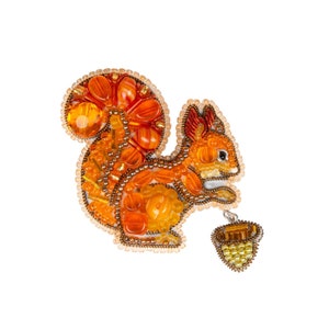 Peut inclure: Une broche en forme d'écureuil en perles, dans des tons orange et jaune. L'écureuil tient un gland en perles dans ses pattes.