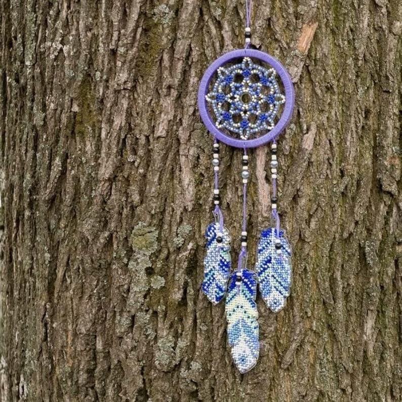 May include: Purple dream catcher with white and blue beaded feathers hanging from a tree trunk.