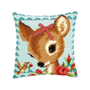 May include: A light blue pillow with a cross-stitch design of a fawn with a red and white polka dot bow. The fawn is surrounded by red roses and a small blue bird.