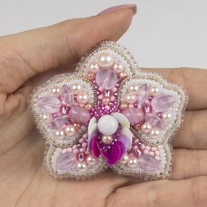 Pu&ograve; includere: Un broche a forma di fiore in perle rosa e bianche con un centro di paillettes rosa. Il broche &egrave; fatto a mano e presenta una variet&agrave; di perle, tra cui perle, perline di vetro e paillettes.