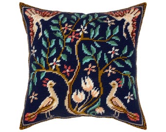 May include: A square needlepoint throw pillow featuring a dark navy blue background with a central tree motif. The design includes two light-colored birds with pink accents at the base, surrounded by green leaves and small pink and white flowers.