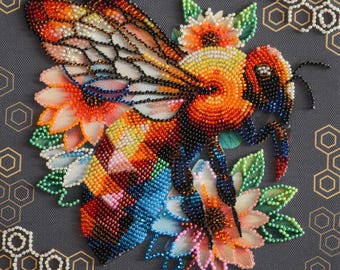 Könnte beinhalten: Ein Perlenstickerei-Kunstwerk mit einer großen Biene mit orangefarbenen, gelben und schwarzen Flügeln und Körper, umgeben von bunten Blüten in Rosa-, Orange- und Grüntönen, vor einem dunkelgrauen Hintergrund mit einem Wabenmuster.