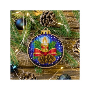 May include: A blue and gold Christmas bauble with a candle and pine cone design. The bauble is decorated with red ribbon and white snowflakes.