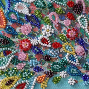 May include: Close-up of a colorful beaded artwork with a floral design. The beads are arranged in a variety of patterns and colors, including red, blue, green, white, and orange. The artwork is created on a canvas background.