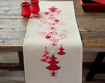 Könnte beinhalten: Ein weißer Tischläufer mit einem roten und weißen gestickten Weihnachtsbaumdesign. Der Läufer liegt auf einem Holztisch mit zwei roten Glaskerzenhaltern.