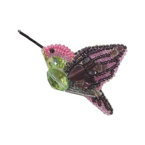Könnte beinhalten: Eine Brosche in Form eines Kolibris aus Perlen, mit rosa, grünen und violetten Perlen. Der Kolibri ist im Flug mit ausgebreiteten Flügeln.