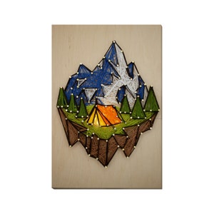 May include: String art depicting a mountain range with a small orange tent in the valley. The mountains are blue, white, and green, and the valley is green. The art is on a wooden background.