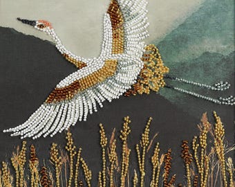 May include: A beaded wall art piece featuring a crane in flight, crafted with white, gold, and brown glass beads. The bird is set against a dark background with beaded stalks of wheat in gold and brown tones, creating a textured, dimensional effect.