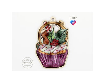 May include: A wooden Christmas ornament shaped like a cupcake with a purple frosting base, green holly leaves, red berries, and a brown chocolate topping. The ornament has a hole at the top for hanging.