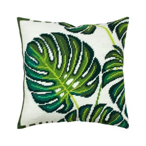 Op de afbeelding: Een vierkant naaldpunt sierkussen met een witte achtergrond en een groot, gedetailleerd monstera-bladpatroon in verschillende tinten groen, waaronder donker bosgroen, smaragd en limoengroen, met een donkergroene gestikte rand.