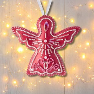 May include: A red angel-shaped Christmas ornament with white beaded accents and a decorative gemstone. The wings and outline are detailed with small white beads. A white ribbon is attached for hanging.