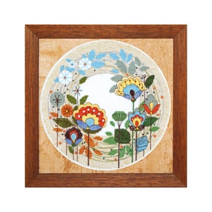 May include: A framed cross-stitch embroidery featuring a circular design of colourful flowers and leaves on a beige background.