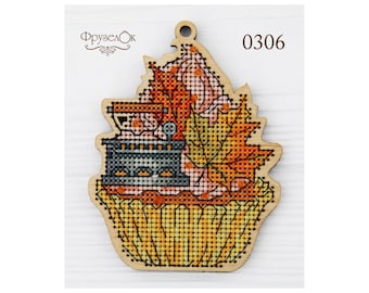 May include: A wooden cross-stitch ornament shaped like a cupcake with a small iron and autumn leaves on top. The ornament is labeled "0306".