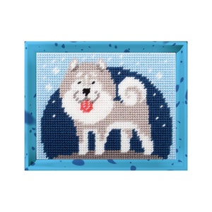 Op de afbeelding: Een ingelijst naaldkunstwerk met een grijs-witte hond met een rode tong, tegen een blauwe en witte achtergrond.