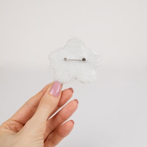 Pu&ograve; includere: Broche a forma di stella in feltro bianco con una spilla argentata sul retro.