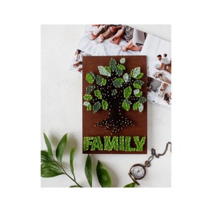 May include: A wooden sign with a string art tree design in shades of green and black. The word "FAMILY" is spelled out below the tree in green string.