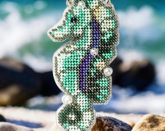 Op de afbeelding: Een kralen-zeepaardje hangerketting met een zilveren ketting en parel accenten. Het zeepaardje is groen, blauw en goud.