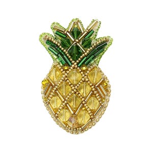 Può includere: Un broche a forma di ananas realizzato con perline, con la parte superiore verde e il corpo giallo. L'ananas è fatto di piccole perline rotonde ed è una rappresentazione realistica di un ananas.