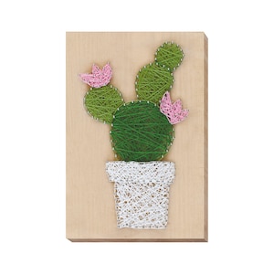 Puede incluir: Un cactus verde de arte de hilo con flores rosas en una maceta blanca sobre un fondo de madera.