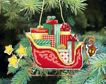 May include: A red and gold sleigh filled with wrapped presents, decorated with stars and a lantern. This is a Christmas ornament.
