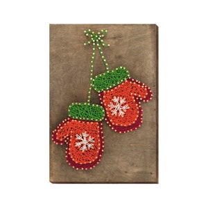 May include: A pair of red mittens with green cuffs and white snowflake designs are strung with yarn on a wooden background.