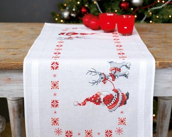 Könnte beinhalten: Weißer Tischläufer mit einem roten und weißen Stickmuster von Weihnachtsmann und Rentier. Das Design enthält Schneeflocken und einen Rand aus kleinen roten und weißen Quadraten.