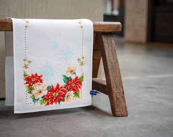 Könnte beinhalten: Ein weißer Tischläufer mit einem roten und weißen Weihnachtsstern-Blumendesign und goldenen Sternen. Der Läufer hängt an einem Holzhocker.