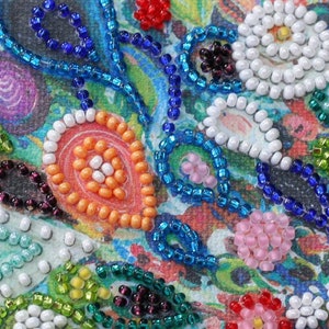 May include: Close-up of a colorful beaded design on a canvas. The design features a variety of shapes and colors, including white, blue, green, orange, and pink.