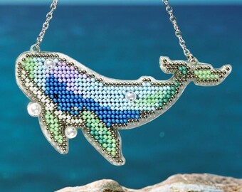 Op de afbeelding: Een kralenketting met een hanger in de vorm van een walvis. De walvis is gemaakt van blauwe, groene en paarse kralen en heeft een witte parel op zijn buik.