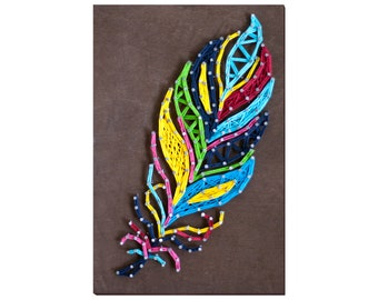 May include: A colourful feather design created with string art on a brown wooden background. The feather is made with blue, green, yellow, red, and black string.