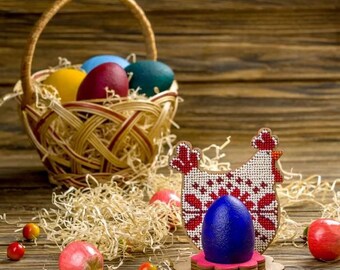 Può includere: Un uovo di Pasqua blu si trova in un porta uova di legno a forma di gallina. Il porta uova è decorato con perline rosse e bianche. La gallina è in piedi su una base rosa. Ci sono altri uova di Pasqua in un cesto di vimini sullo sfondo.