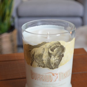 May include: A clear glass candle jar with a white candle and a label that says "Buffalo Trace Kentucky Straight Bourbon Whiskey". The label features a drawing of a buffalo.