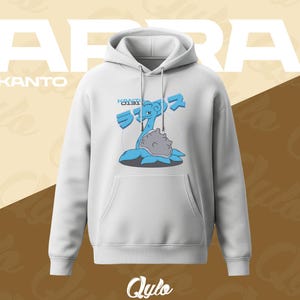 Puede incluir: Sudadera con capucha blanca con bolsillo delantero y capucha. La sudadera presenta un gr&aacute;fico azul y gris de una criatura con el texto "KANTO" y caracteres japoneses. La palabra "LAPRAS" est&aacute; impresa en letras blancas grandes encima.