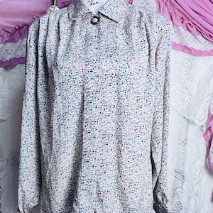 Könnte beinhalten: Ein Vintage-Hemd mit Knopfleiste und einem gesprenkelten Muster in Weiß, Schwarz, Rosa und Türkis. Das langärmlige Hemd hat einen Kragen und einen einzelnen Knopfverschluss. Das Hemd wird auf einer Schaufensterpuppe präsentiert.